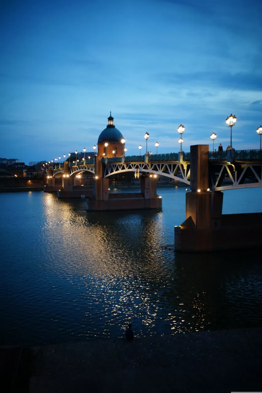 Pont illuminé sur une rivière le soir.